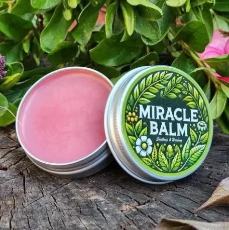 Miracle Balm soothing lip balm in tin with green leaf label, set on rustic wood amid greenery